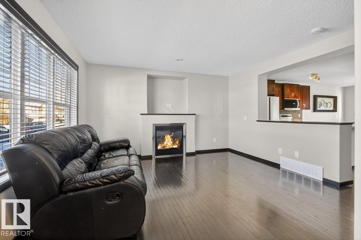 Living room featuring a glass covered fireplace, hardwood / wood-style flooring, and a textured ceiling - 3623 13 Street, Edmonton, AB - Indoor Photo Showing Living Room With Fireplace