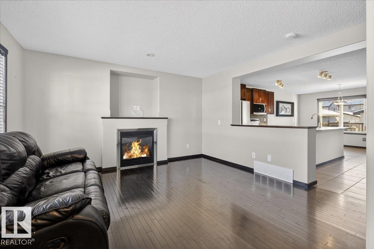 Living room featuring a glass covered fireplace, a textured ceiling, and dark wood finished floors - 3623 13 Street, Edmonton, AB - Indoor Photo Showing Living Room With Fireplace