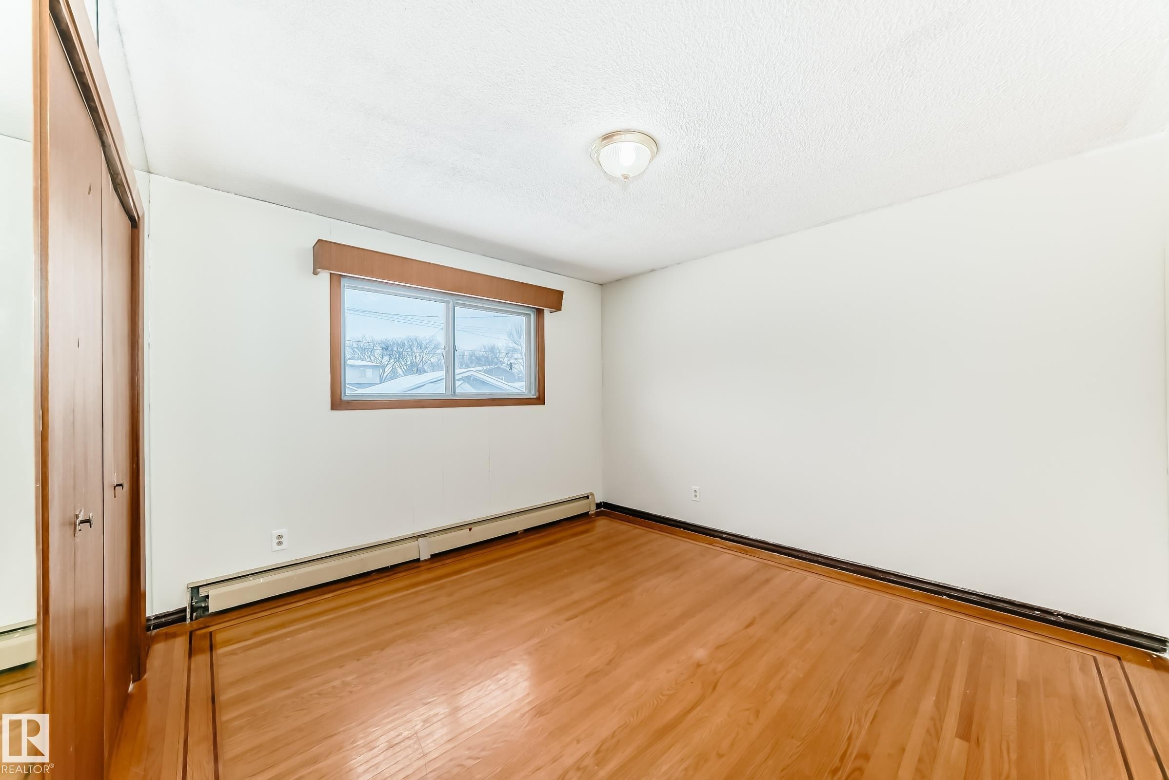 Unfurnished bedroom featuring a baseboard heating unit, wood finished floors, a closet, a baseboard radiator, and a textured ceiling - 12028 87 Street, Edmonton, AB - Indoor Photo Showing Other Room
