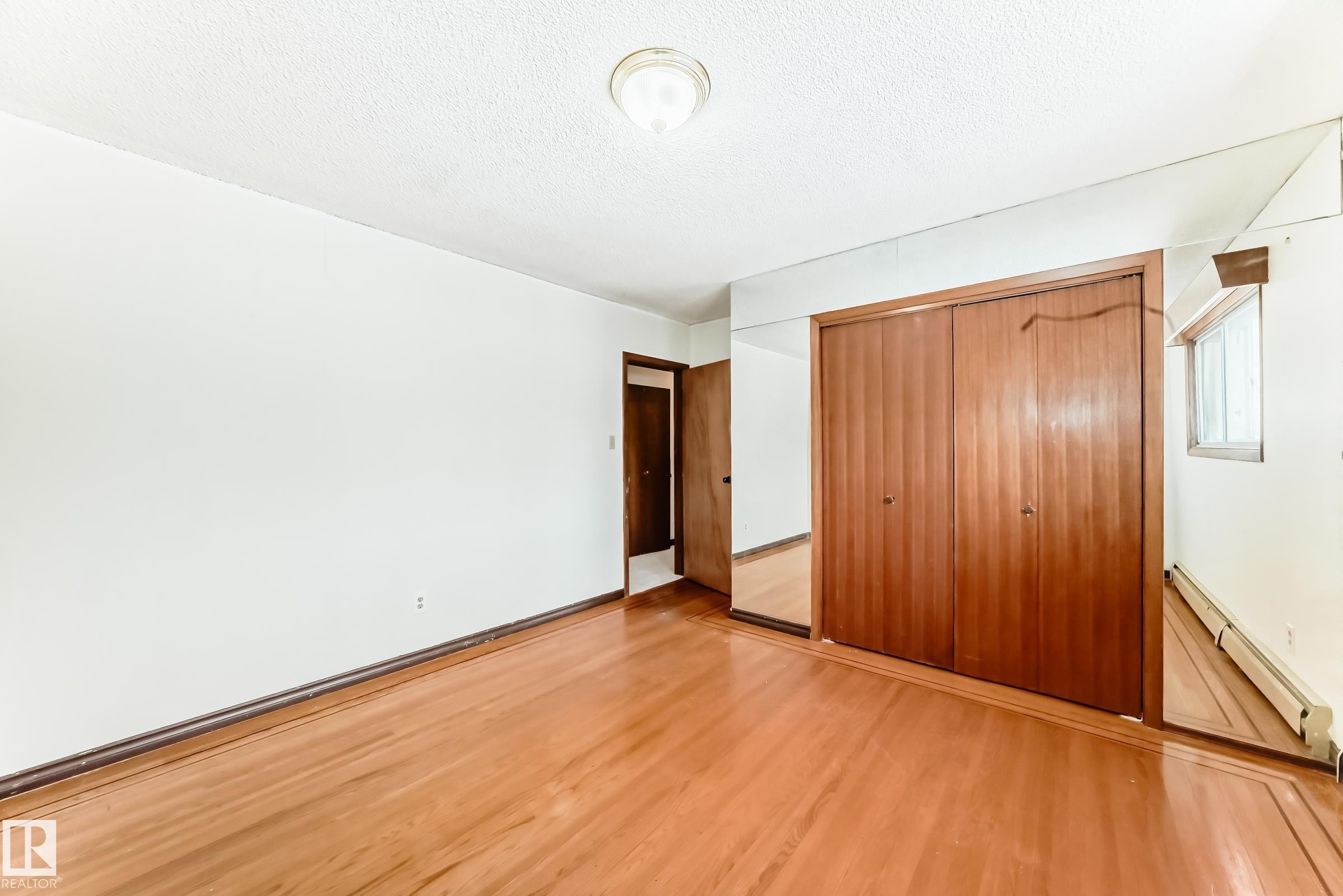 Unfurnished bedroom featuring baseboard heating, a closet, light wood-style flooring, and a textured ceiling - 12028 87 Street, Edmonton, AB - Indoor Photo Showing Other Room