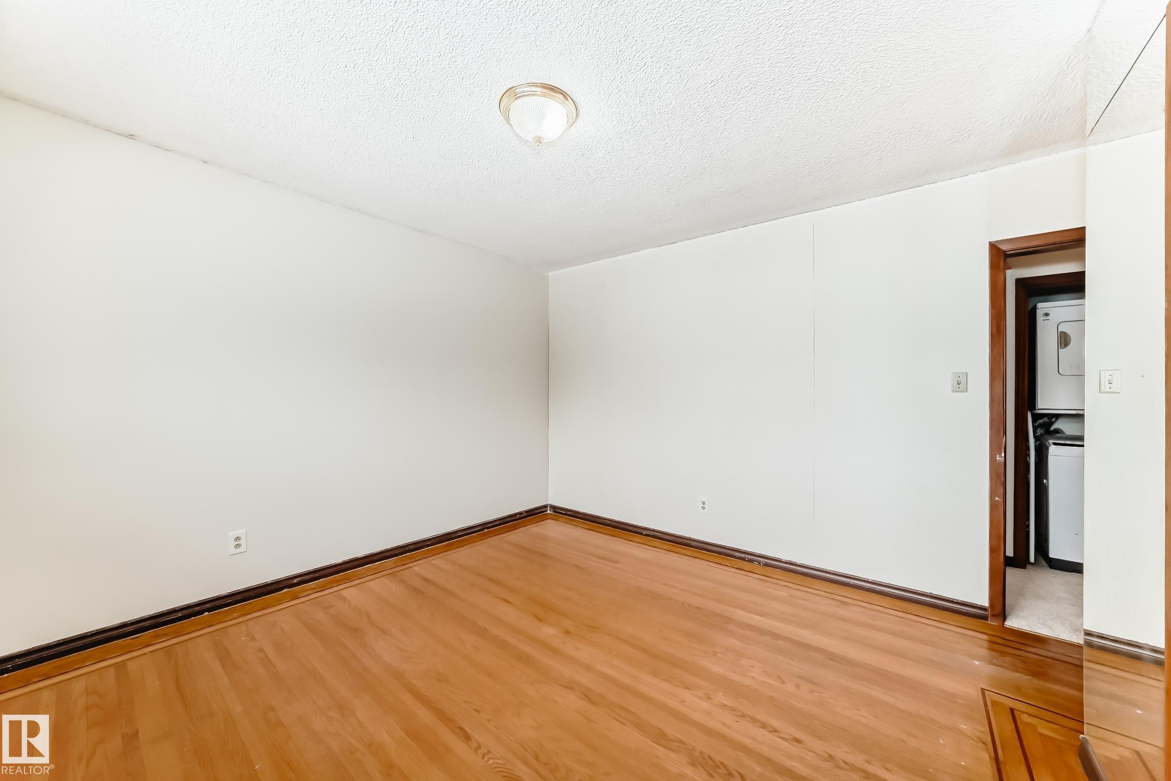 Spare room featuring stacked washer / dryer, wood finished floors, and a textured ceiling - 12028 87 Street, Edmonton, AB - Indoor Photo Showing Other Room