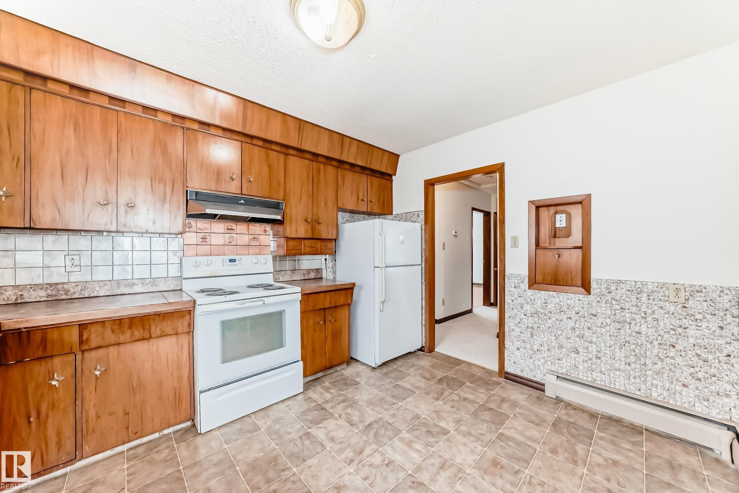 Kitchen with white appliances, brown cabinets, light countertops, a baseboard radiator, and under cabinet range hood - 12028 87 Street, Edmonton, AB - Indoor Photo Showing Kitchen