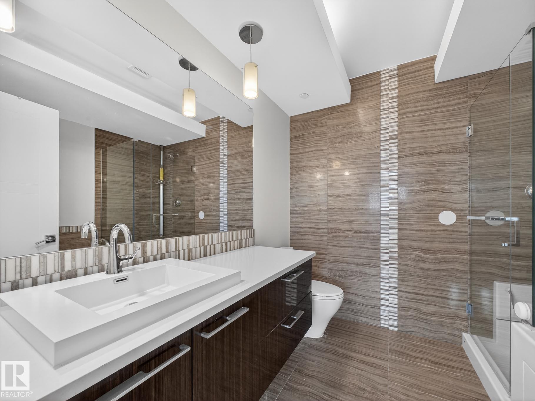 Full bath featuring tile walls, vanity, a stall shower, and dark tile patterned flooring - #902 11969 Jasper Av Nw, Edmonton, AB - Indoor Photo Showing Bathroom