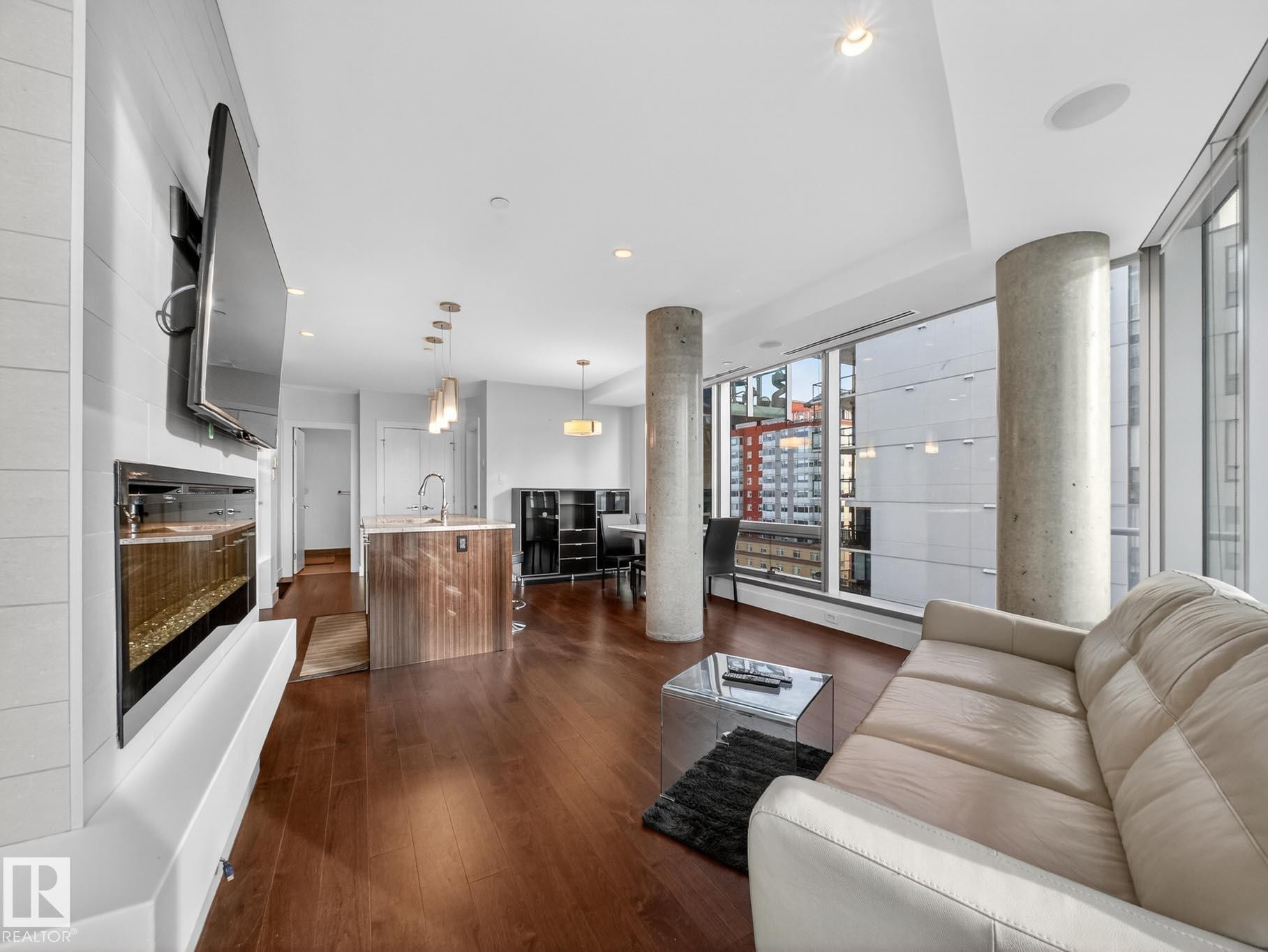 Living room featuring dark wood-style flooring, recessed lighting, and expansive windows - #902 11969 Jasper Av Nw, Edmonton, AB - Indoor Photo Showing Living Room With Fireplace
