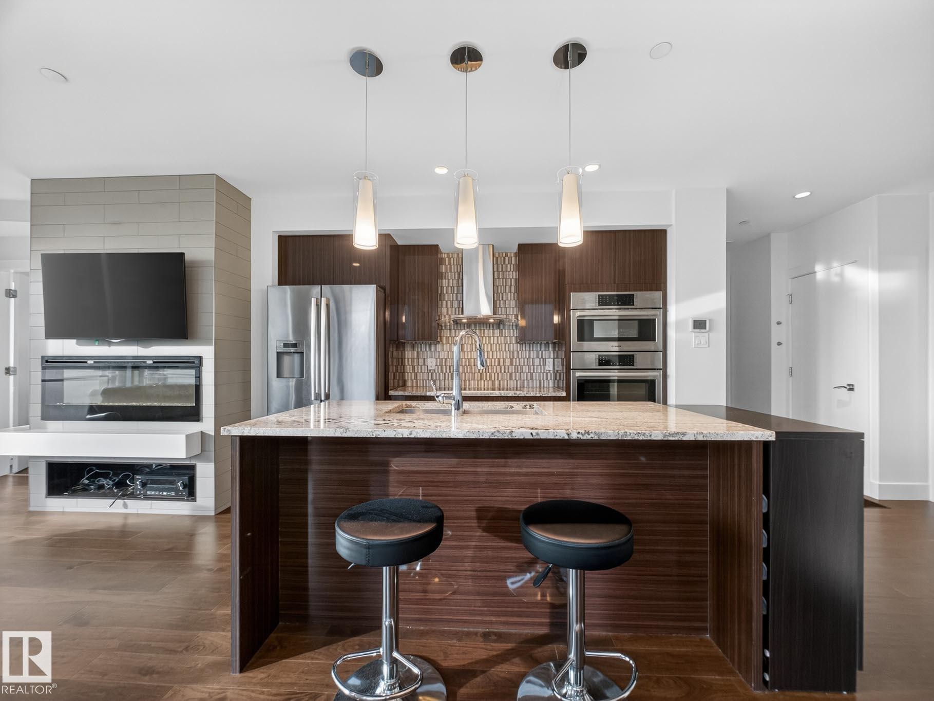 Kitchen featuring dark brown cabinetry, light stone countertops, a kitchen bar, decorative backsplash, and modern cabinets - #902 11969 Jasper Av Nw, Edmonton, AB - Indoor Photo Showing Kitchen With Stainless Steel Kitchen With Upgraded Kitchen