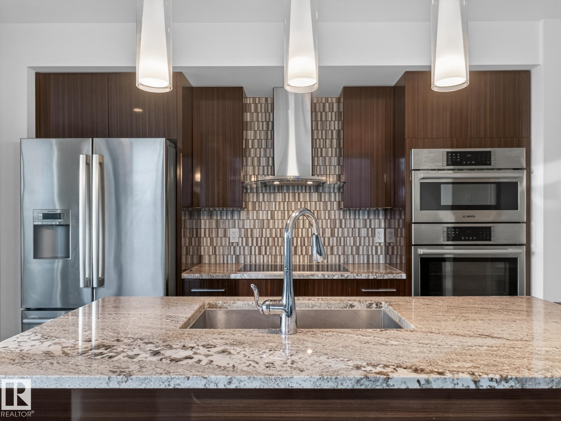 Kitchen featuring light stone countertops, stainless steel appliances, dark brown cabinets, modern cabinets, and wall chimney range hood - #902 11969 Jasper Av Nw, Edmonton, AB - Indoor Photo Showing Kitchen With Stainless Steel Kitchen With Double Sink With Upgraded Kitchen