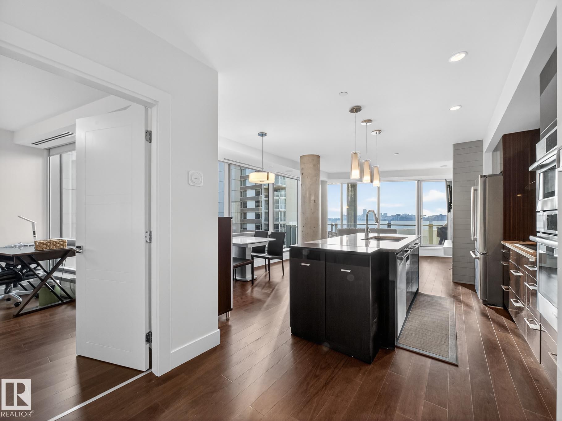 Kitchen featuring modern cabinets, decorative light fixtures, a center island with sink, dark wood-type flooring, and stainless steel appliances - #902 11969 Jasper Av Nw, Edmonton, AB - Indoor Photo Showing Kitchen With Upgraded Kitchen