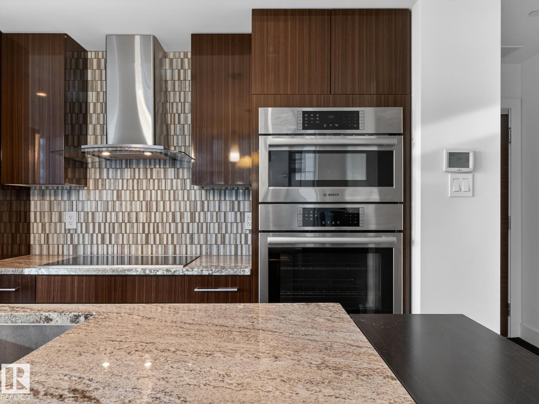 Kitchen featuring double oven, modern cabinets, wall chimney range hood, backsplash, and light stone countertops - #902 11969 Jasper Av Nw, Edmonton, AB - Indoor Photo Showing Kitchen With Stainless Steel Kitchen