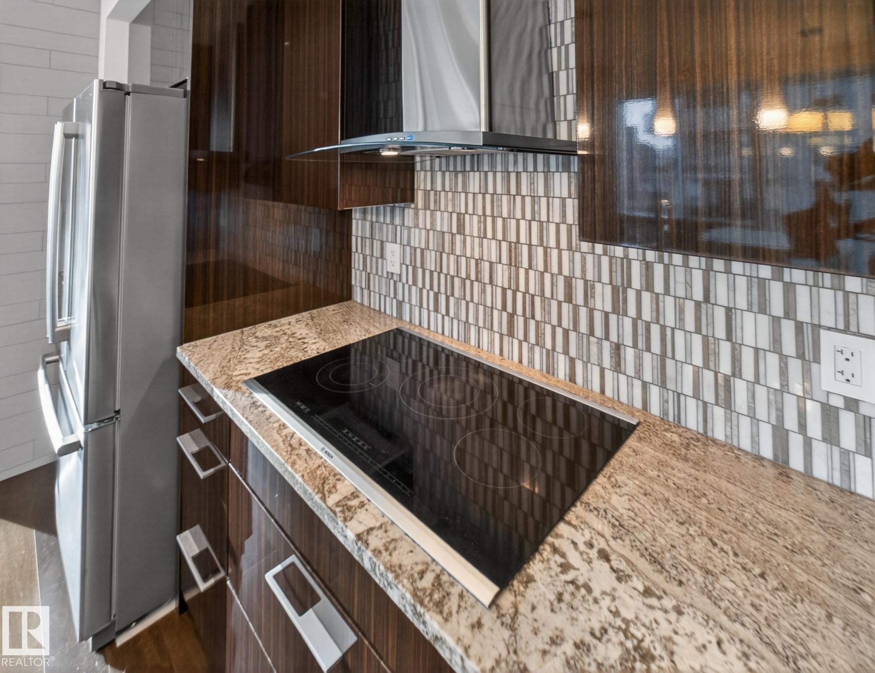Kitchen with black electric stovetop, wall chimney exhaust hood, light stone countertops, modern cabinets, and freestanding refrigerator - #902 11969 Jasper Av Nw, Edmonton, AB - Indoor Photo Showing Kitchen