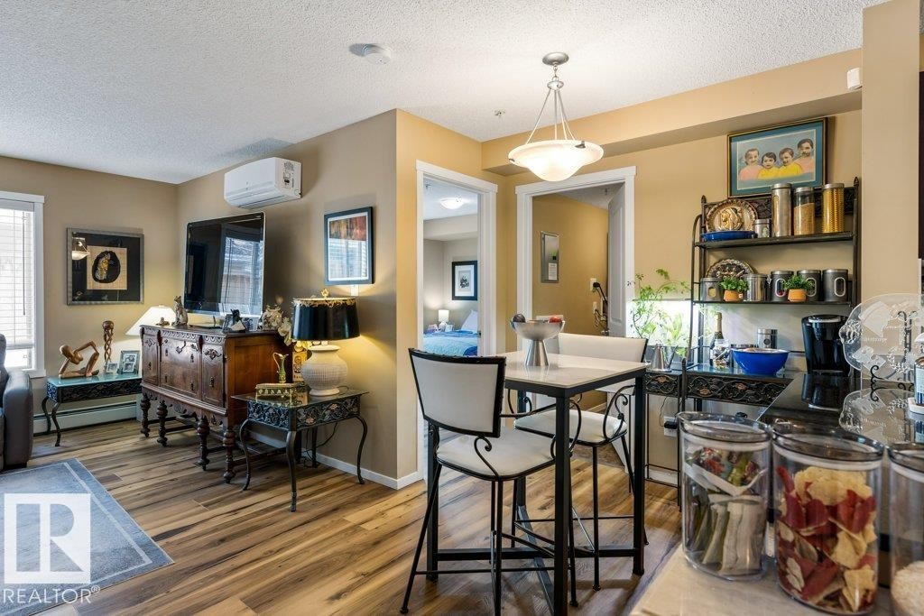 Dining space featuring a textured ceiling, wood finished floors, an AC wall unit, and baseboard heating - 107 25 Element Dr, St. Albert, AB - Indoor