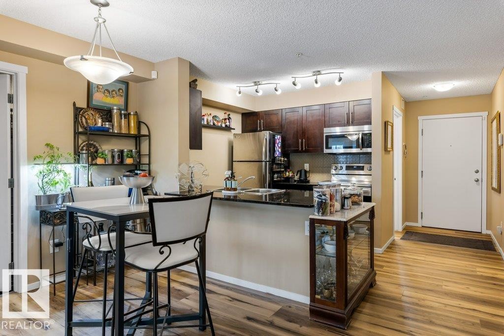 Kitchen with dark brown cabinetry, decorative backsplash, appliances with stainless steel finishes, pendant lighting, and a peninsula - 107 25 Element Dr, St. Albert, AB - Indoor Photo Showing Kitchen