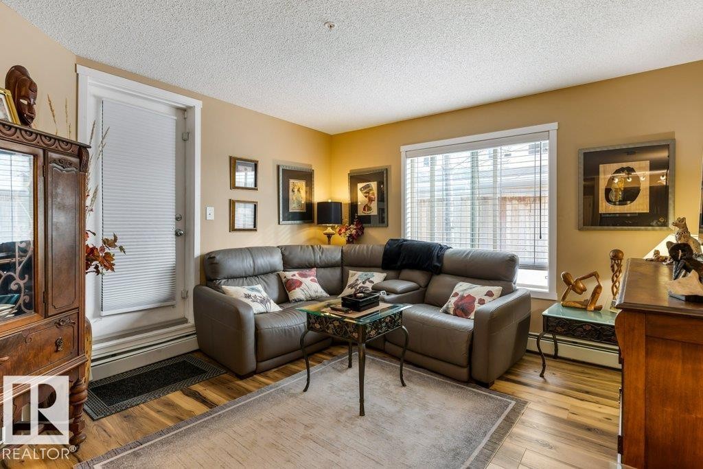 Living area with a textured ceiling, wood-type flooring, and a baseboard heating unit - 107 25 Element Dr, St. Albert, AB - Indoor Photo Showing Living Room