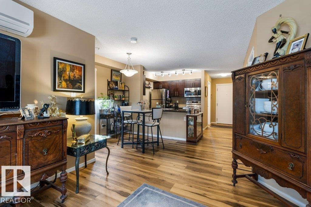 Living room featuring a wall mounted AC, light wood-style floors, and a textured ceiling - 107 25 Element Dr, St. Albert, AB - Indoor