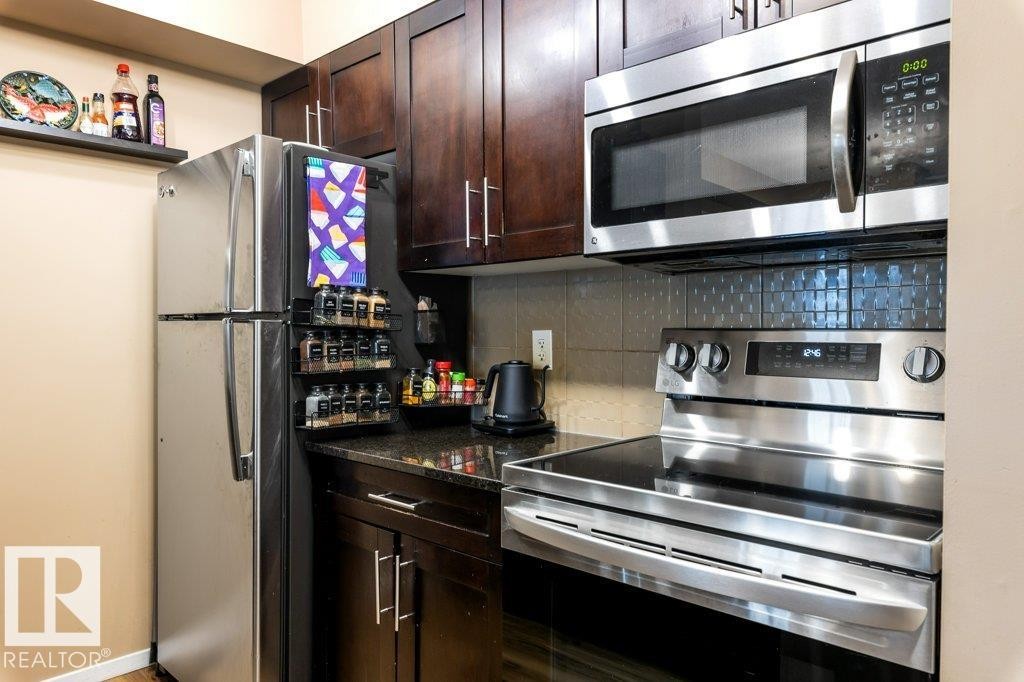 Kitchen with stainless steel appliances, decorative backsplash, dark brown cabinets, and dark stone counters - 107 25 Element Dr, St. Albert, AB - Indoor Photo Showing Kitchen