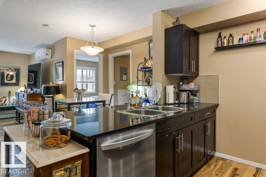 Kitchen featuring light wood finished floors, dark brown cabinetry, stainless steel dishwasher, backsplash, and a peninsula - 107 25 Element Dr, St. Albert, AB - Indoor Photo Showing Kitchen With Double Sink