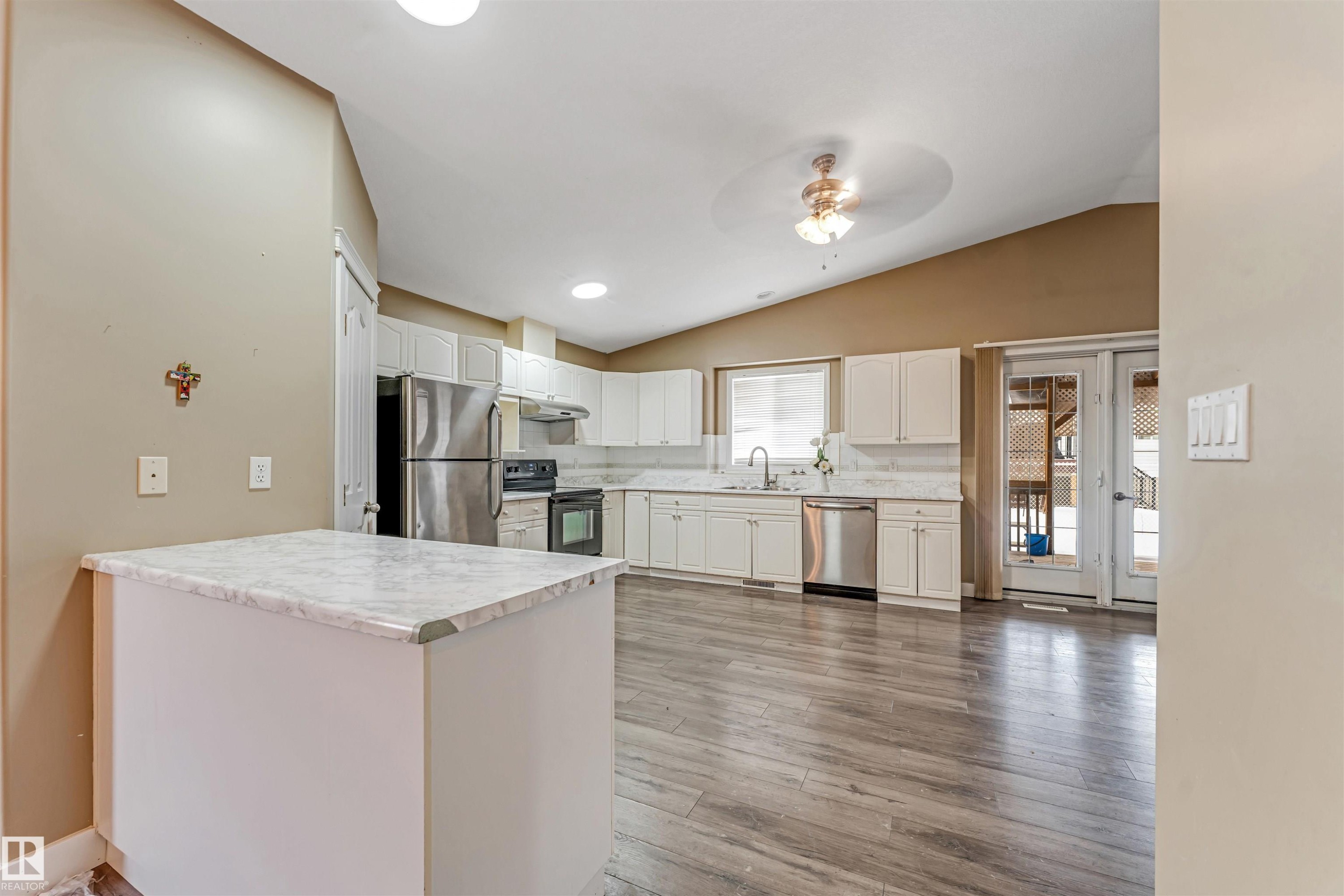 Kitchen with stainless steel appliances, light countertops, light wood-style floors, white cabinets, and vaulted ceiling - 6741 162A Avenue, Edmonton, AB - Indoor Photo Showing Kitchen