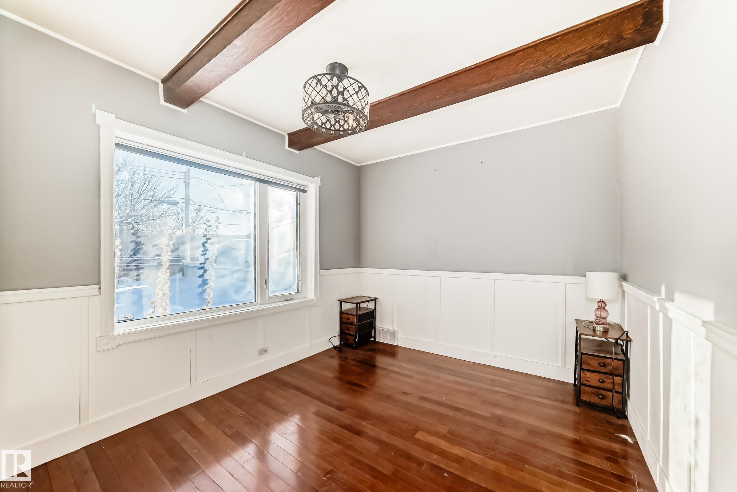 Empty room with wainscoting, dark wood-style flooring, beam ceiling, and a decorative wall - 10115 104, Westlock, AB - Indoor Photo Showing Other Room