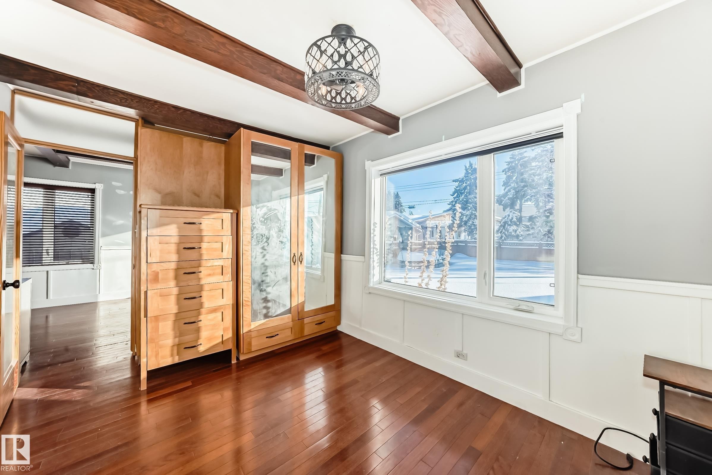 Unfurnished bedroom featuring a wainscoted wall, beam ceiling, wood-type flooring, and a decorative wall - 10115 104, Westlock, AB - Indoor Photo Showing Other Room