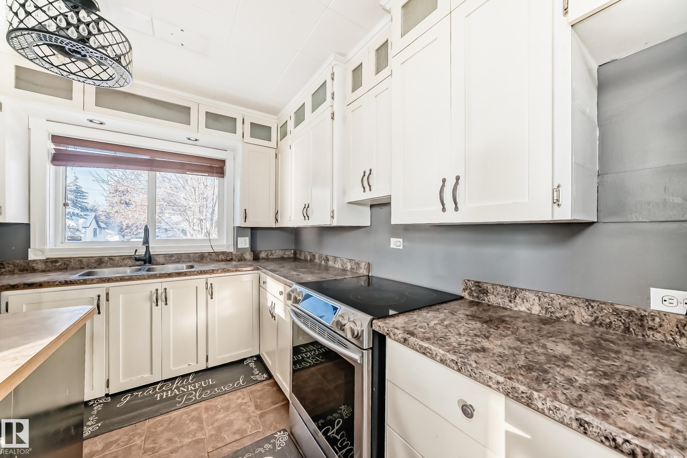 Kitchen with electric range, white cabinets, glass insert cabinets, and dark countertops - 10115 104, Westlock, AB - Indoor Photo Showing Kitchen With Double Sink