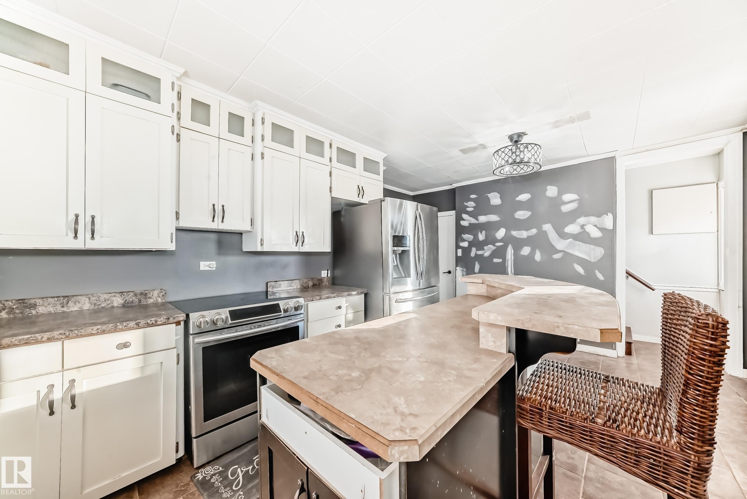 Kitchen with stainless steel appliances, white cabinetry, a kitchen island, glass insert cabinets, and light countertops - 10115 104, Westlock, AB - Indoor Photo Showing Kitchen