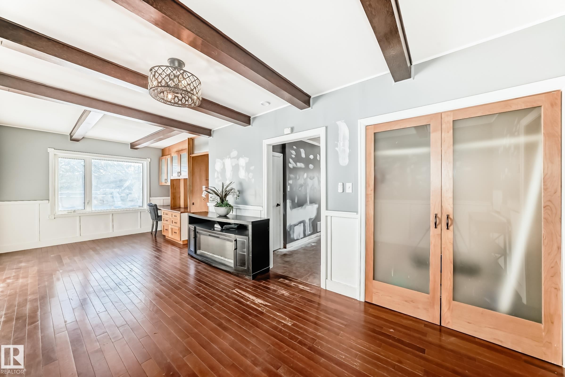 Unfurnished living room with a decorative wall, a wainscoted wall, beamed ceiling, dark wood-style floors, and french doors - 10115 104, Westlock, AB - Indoor Photo Showing Other Room