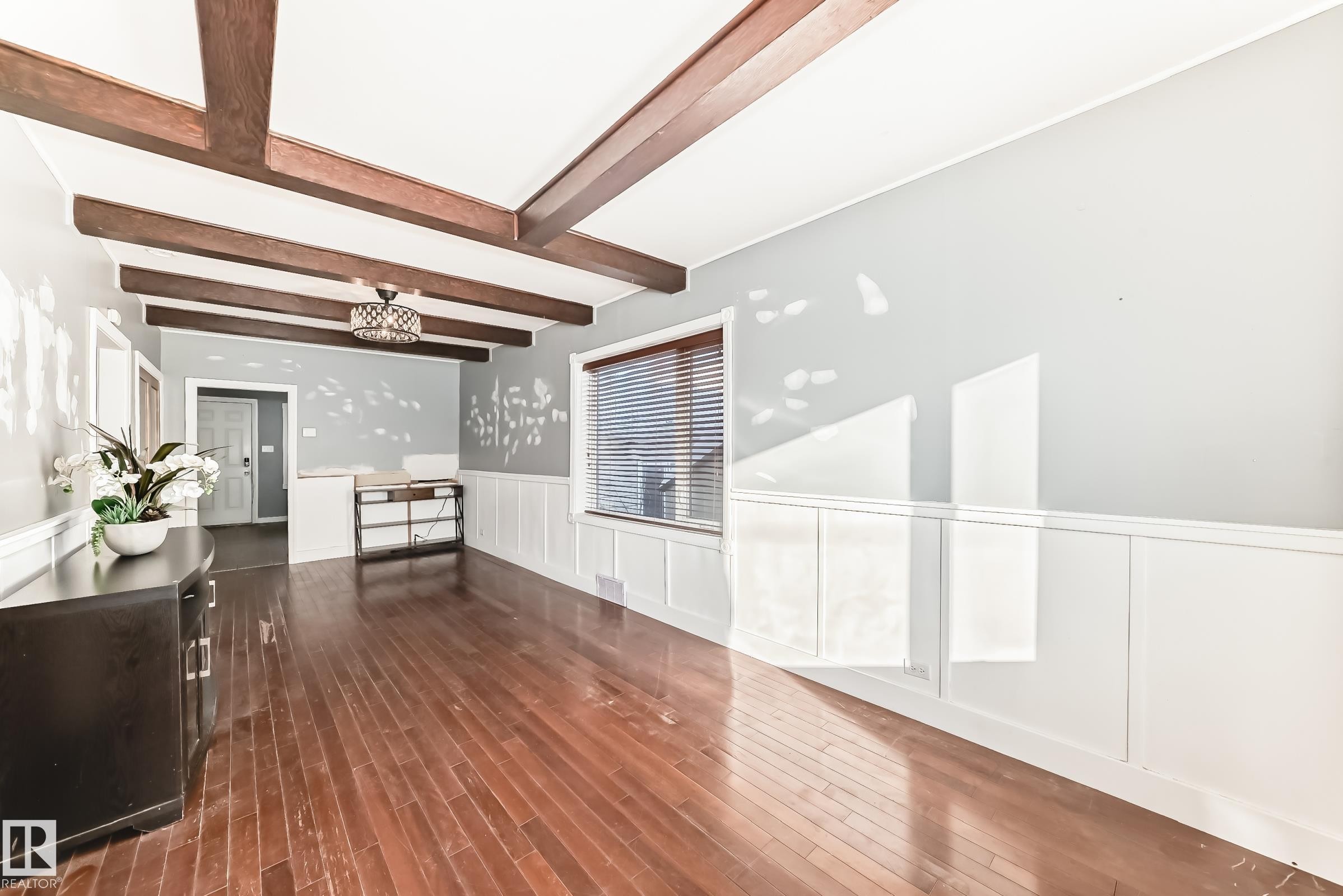 Unfurnished living room with wainscoting, a decorative wall, dark wood finished floors, and beam ceiling - 10115 104, Westlock, AB - Indoor Photo Showing Other Room