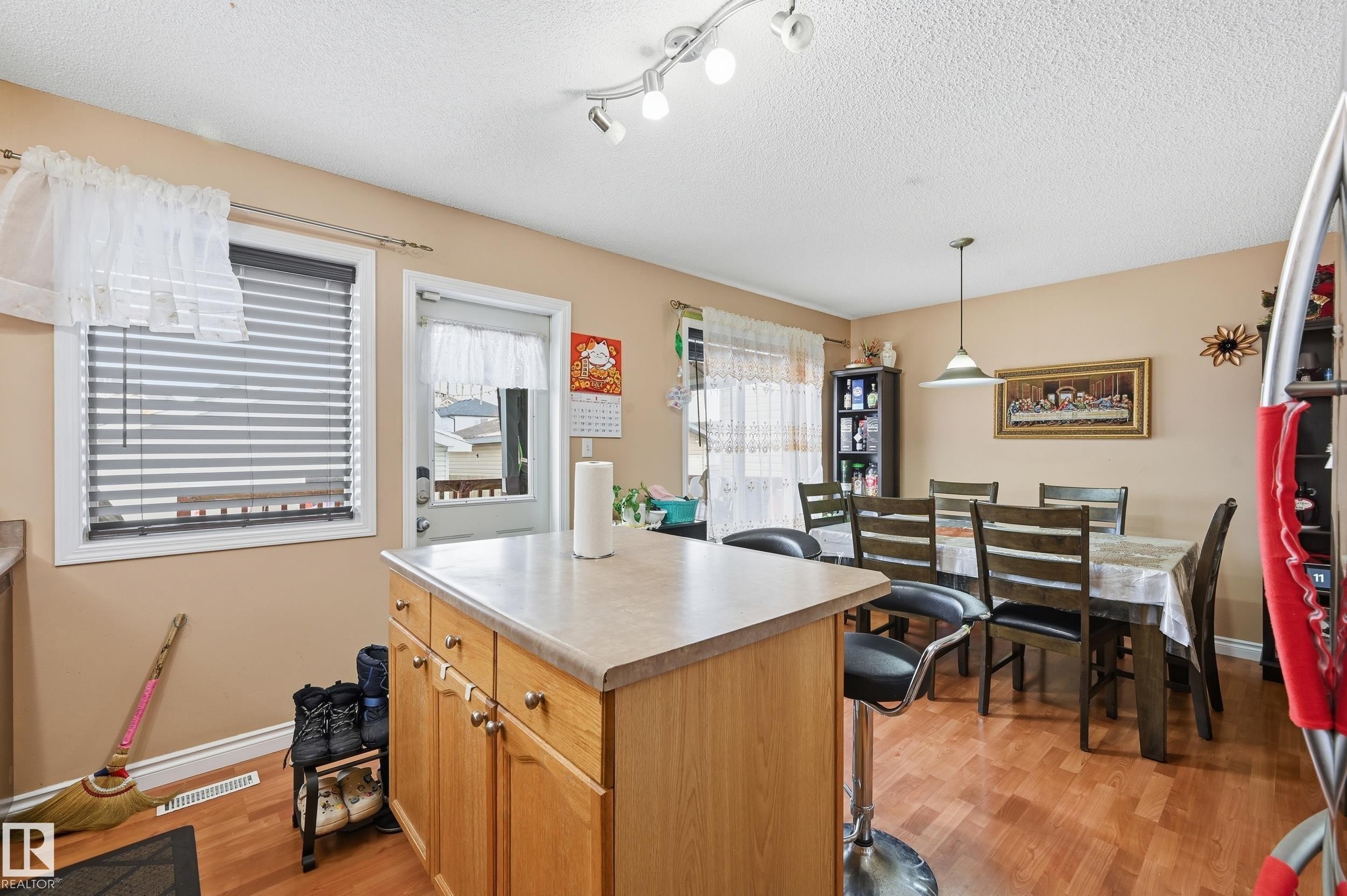 Kitchen with light countertops, light wood-style flooring, a textured ceiling, pendant lighting, and a kitchen island - 3010 32 Avenue Nw, Edmonton, AB - Indoor