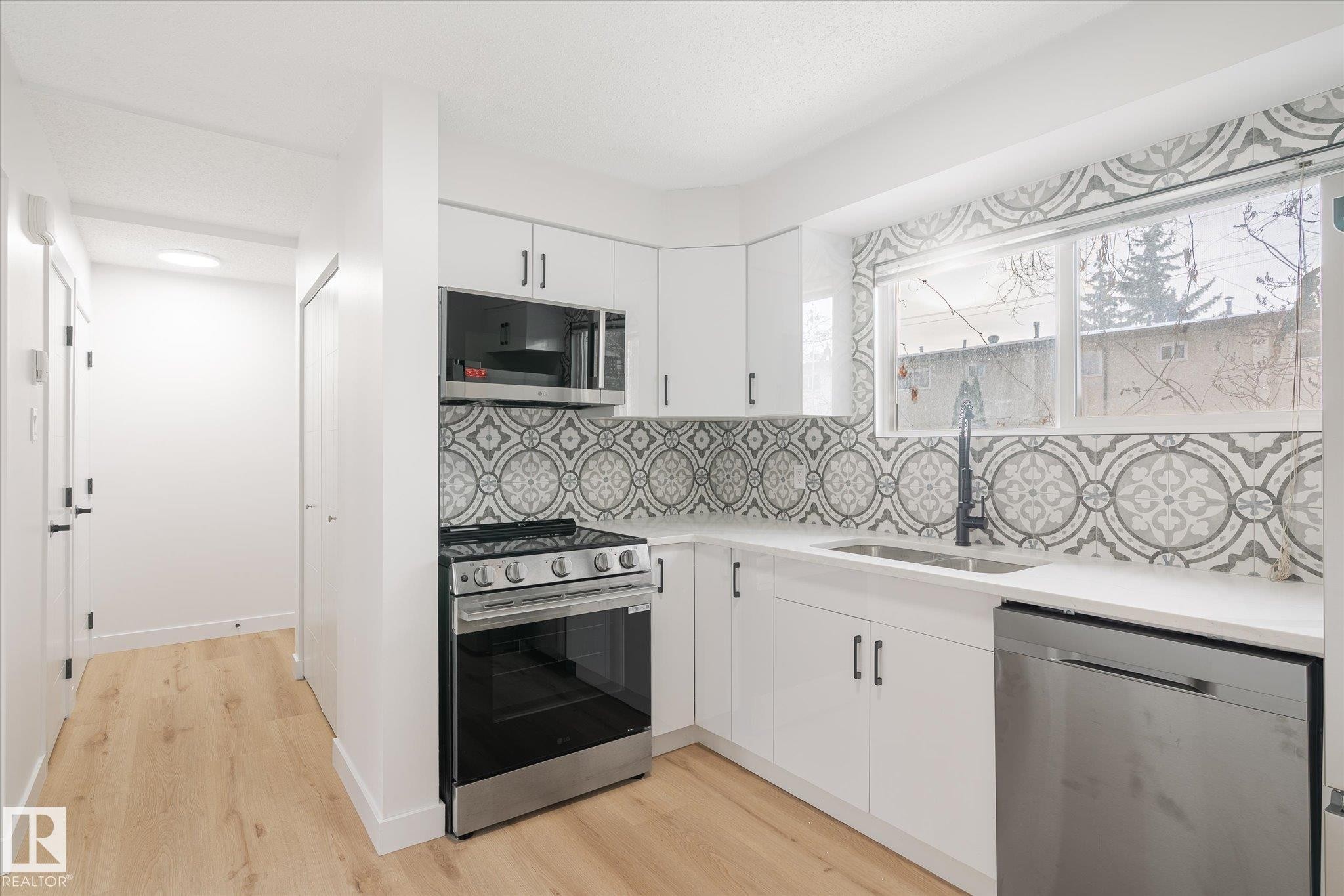 Kitchen featuring stainless steel appliances, light wood-style floors, white cabinetry, and tasteful backsplash - 5105 106A Street, Edmonton, AB - Indoor Photo Showing Kitchen