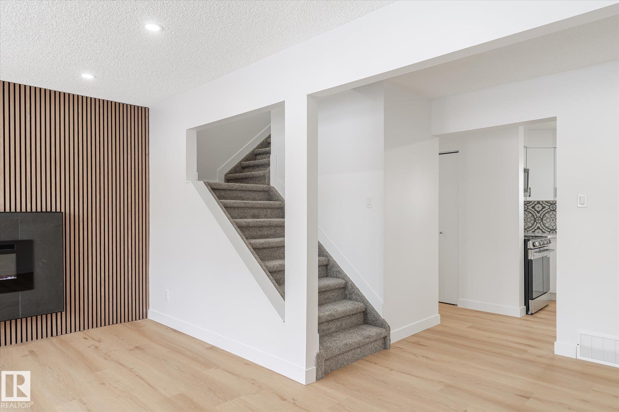 Basement featuring an accent wall, stairway, light wood-style floors, a textured ceiling, and recessed lighting - 5105 106A Street, Edmonton, AB - Indoor Photo Showing Other Room