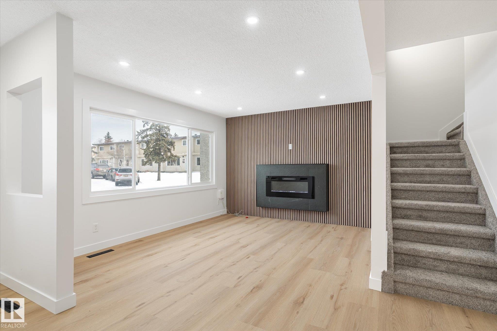 Unfurnished living room featuring an accent wall, light wood finished floors, wooden walls, a textured ceiling, and recessed lighting - 5105 106A Street, Edmonton, AB - Indoor Photo Showing Other Room With Fireplace