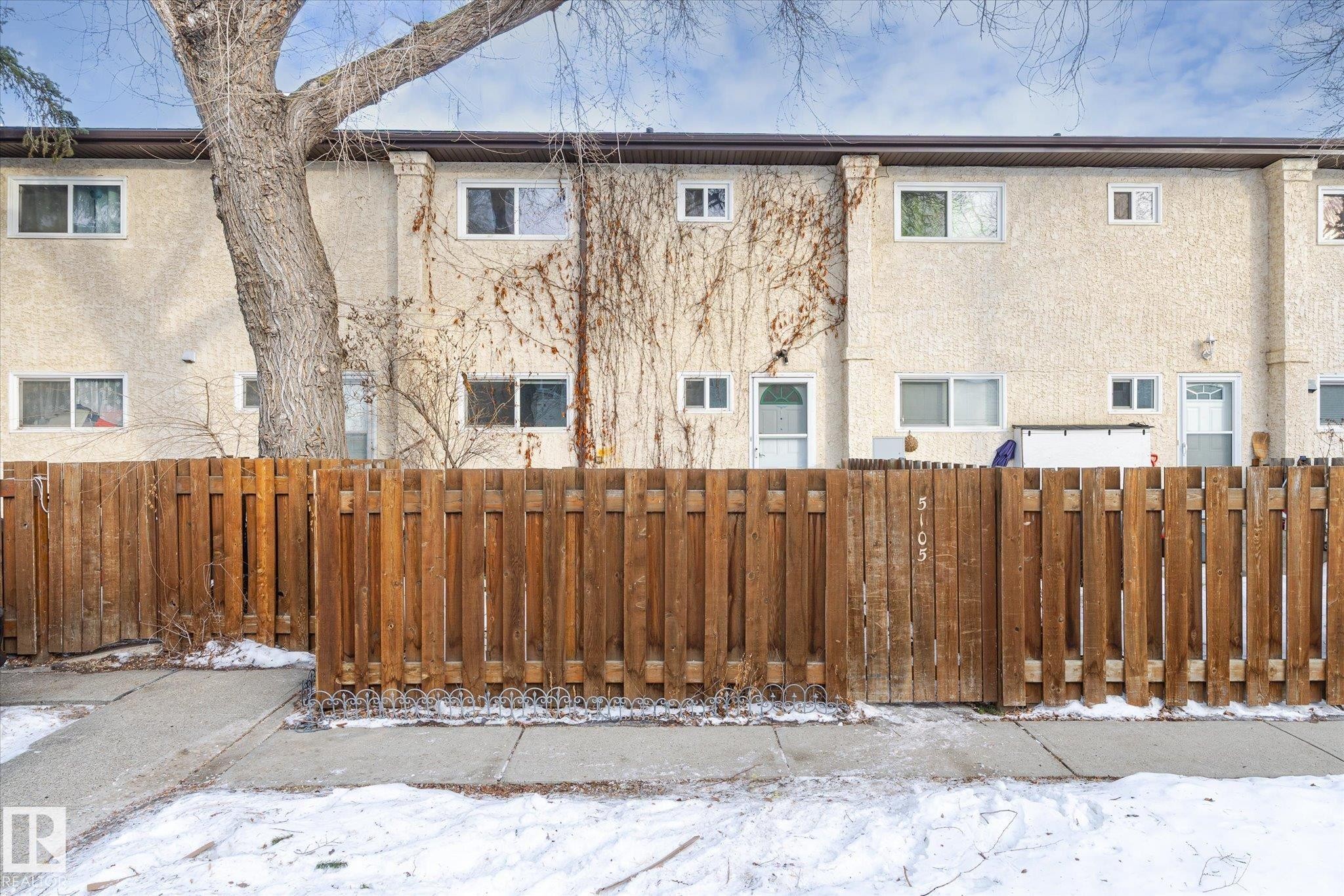 Snow covered house featuring a fenced front yard, stucco siding, and a gate - 5105 106A Street, Edmonton, AB - Outdoor