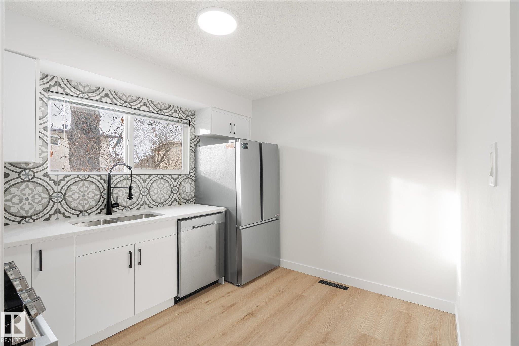 Kitchen featuring white cabinetry, appliances with stainless steel finishes, light wood-style flooring, backsplash, and light stone countertops - 5105 106A Street, Edmonton, AB - Indoor