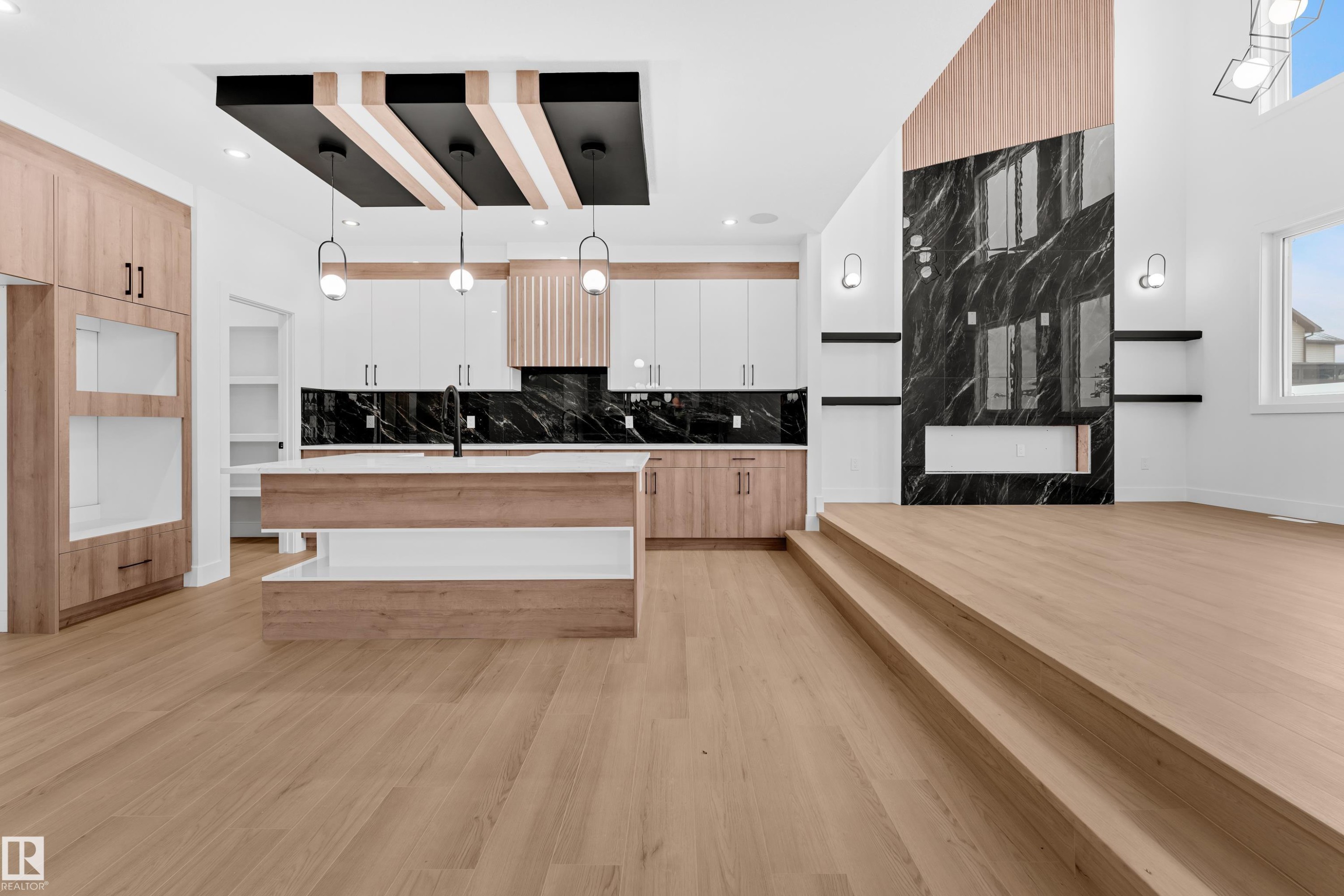 Two tone kitchen featuring decorative light fixtures, a center island with sink, light wood finished floors, decorative backsplash, and modern cabinets - 733 Astoria Way, Devon, AB - Indoor