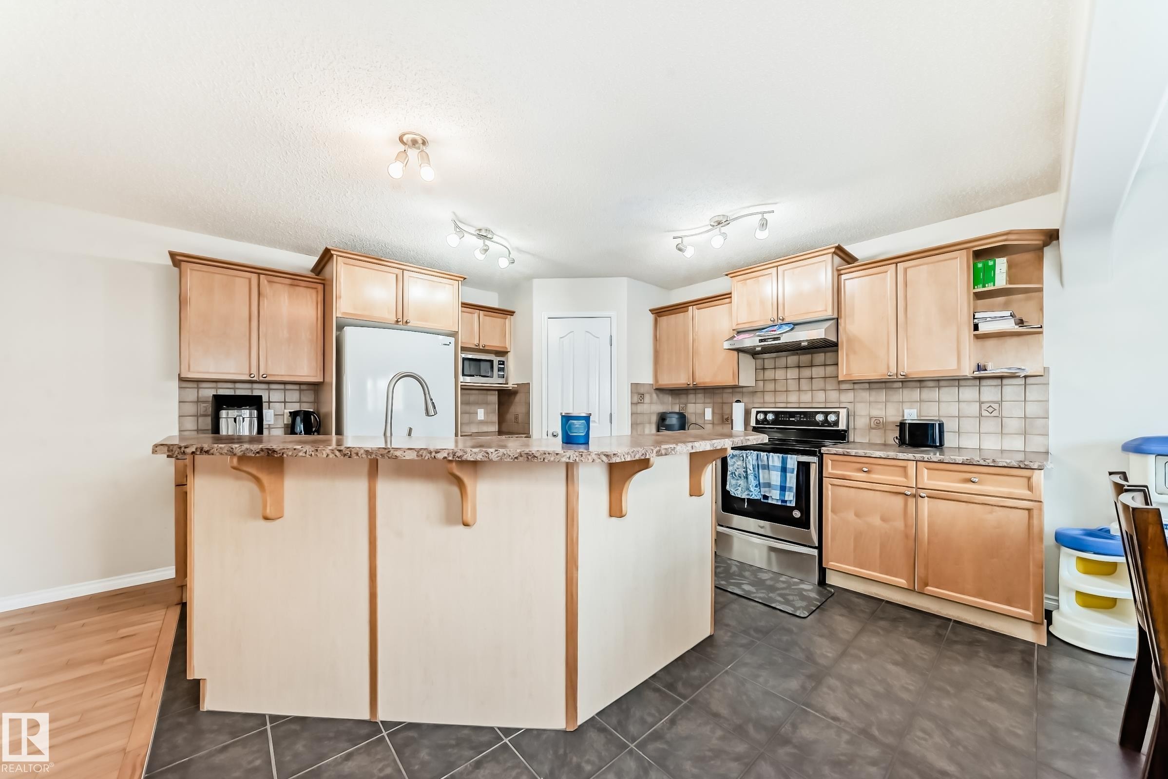 Kitchen featuring a breakfast bar area, light wood finish cabinetry, open shelves, and stainless steel appliances - 5814 165 Avenue, Edmonton, AB - Indoor Photo Showing Kitchen With Stainless Steel Kitchen