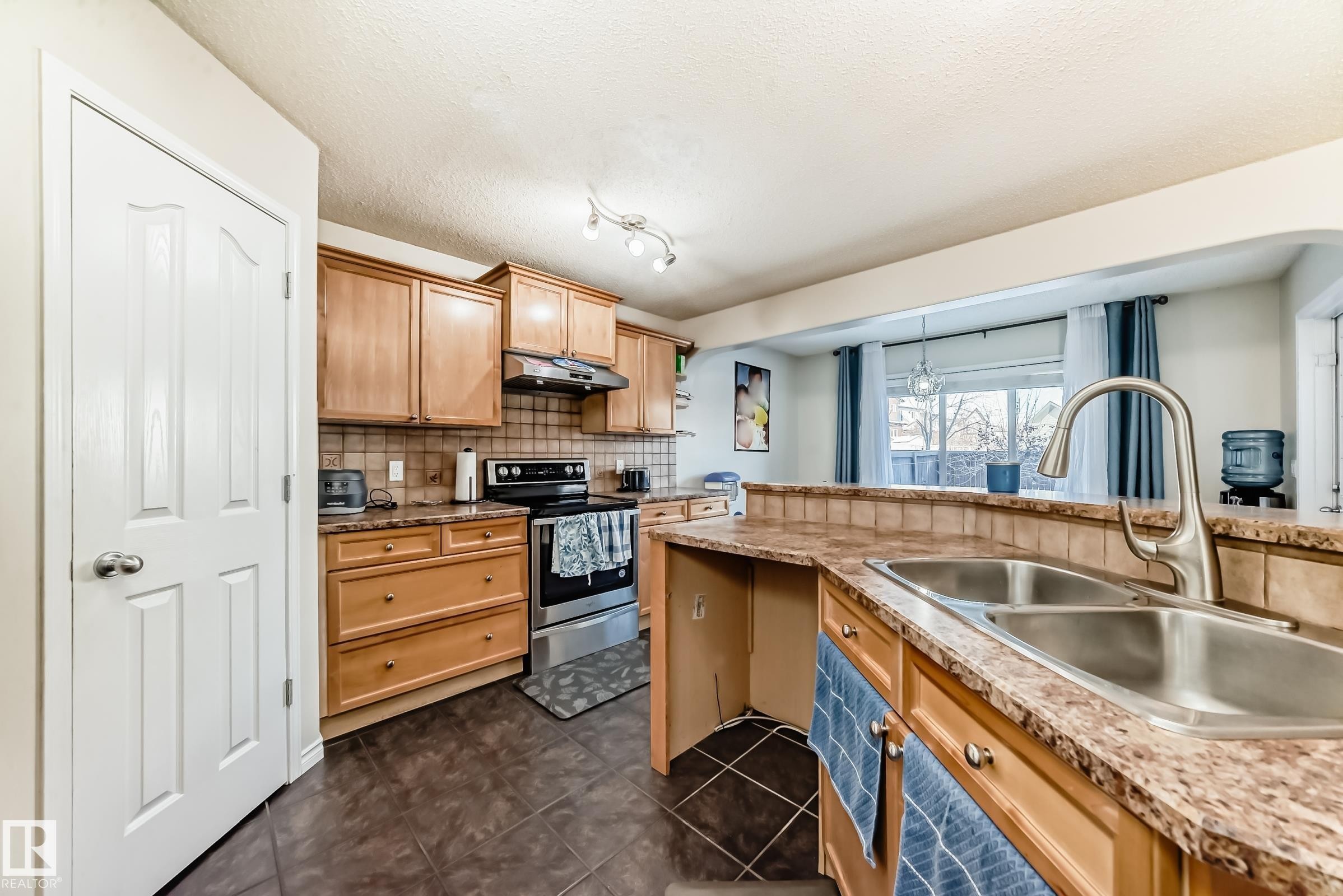 Kitchen with stainless steel electric range, tasteful backsplash, a textured ceiling, and dark tile patterned floors - 5814 165 Avenue, Edmonton, AB - Indoor Photo Showing Kitchen With Double Sink