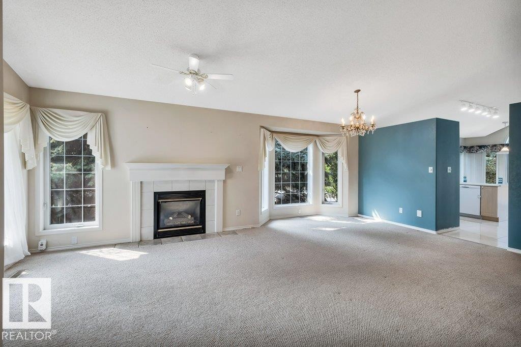 Unfurnished living room featuring carpet flooring, a textured ceiling, a tiled fireplace, suspended lighting, and a ceiling fan - 112 Haddow Close, Edmonton, AB - Indoor Photo Showing Living Room With Fireplace