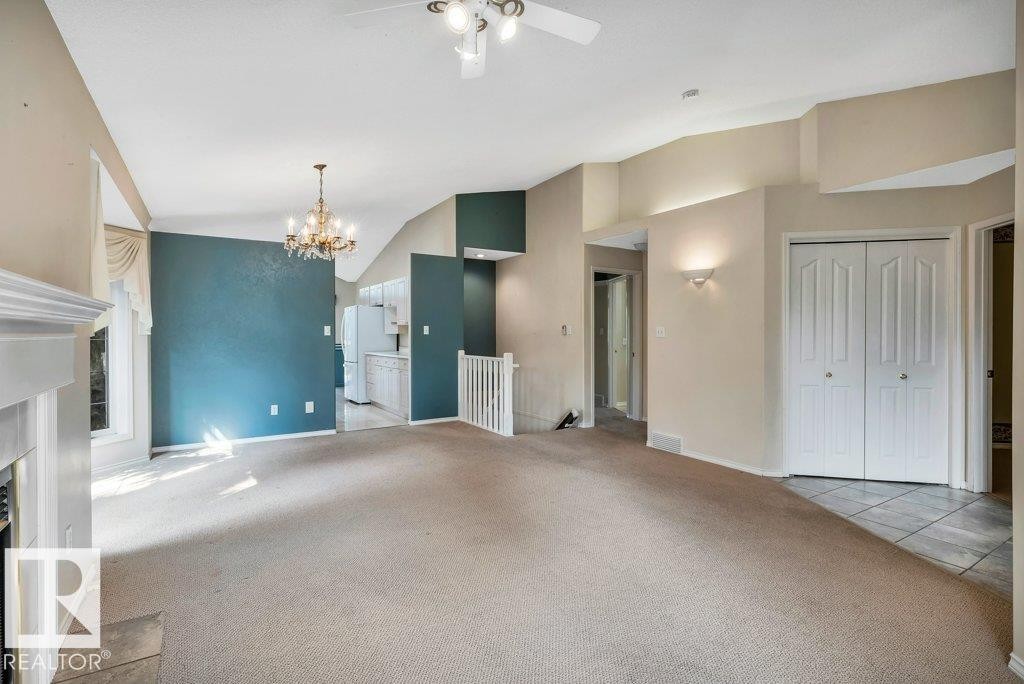 Unfurnished living room featuring vaulted ceiling, carpet floors, a fireplace with flush hearth, suspended lighting, and ceiling fan - 112 Haddow Close, Edmonton, AB - Indoor Photo Showing Other Room