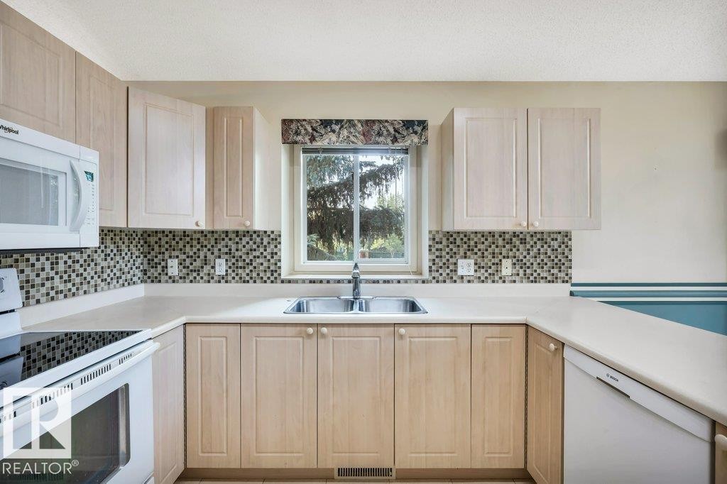 Kitchen with white appliances, light wood finish cabinetry, light countertops, and tasteful backsplash - 112 Haddow Close, Edmonton, AB - Indoor Photo Showing Kitchen With Double Sink
