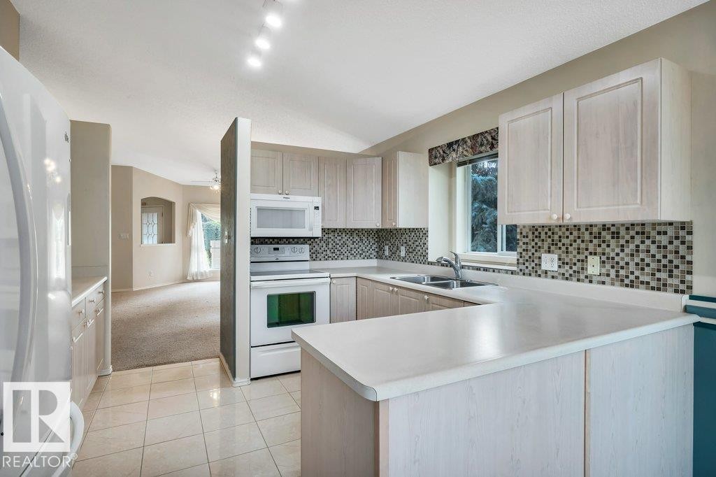 Kitchen featuring white appliances, a peninsula, light countertops, light colored carpet, and decorative backsplash - 112 Haddow Close, Edmonton, AB - Indoor Photo Showing Kitchen With Double Sink