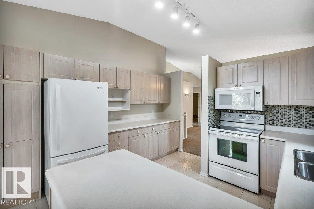 Kitchen featuring white appliances, vaulted ceiling, light countertops, open shelves, and decorative backsplash - 112 Haddow Close, Edmonton, AB - Indoor Photo Showing Kitchen
