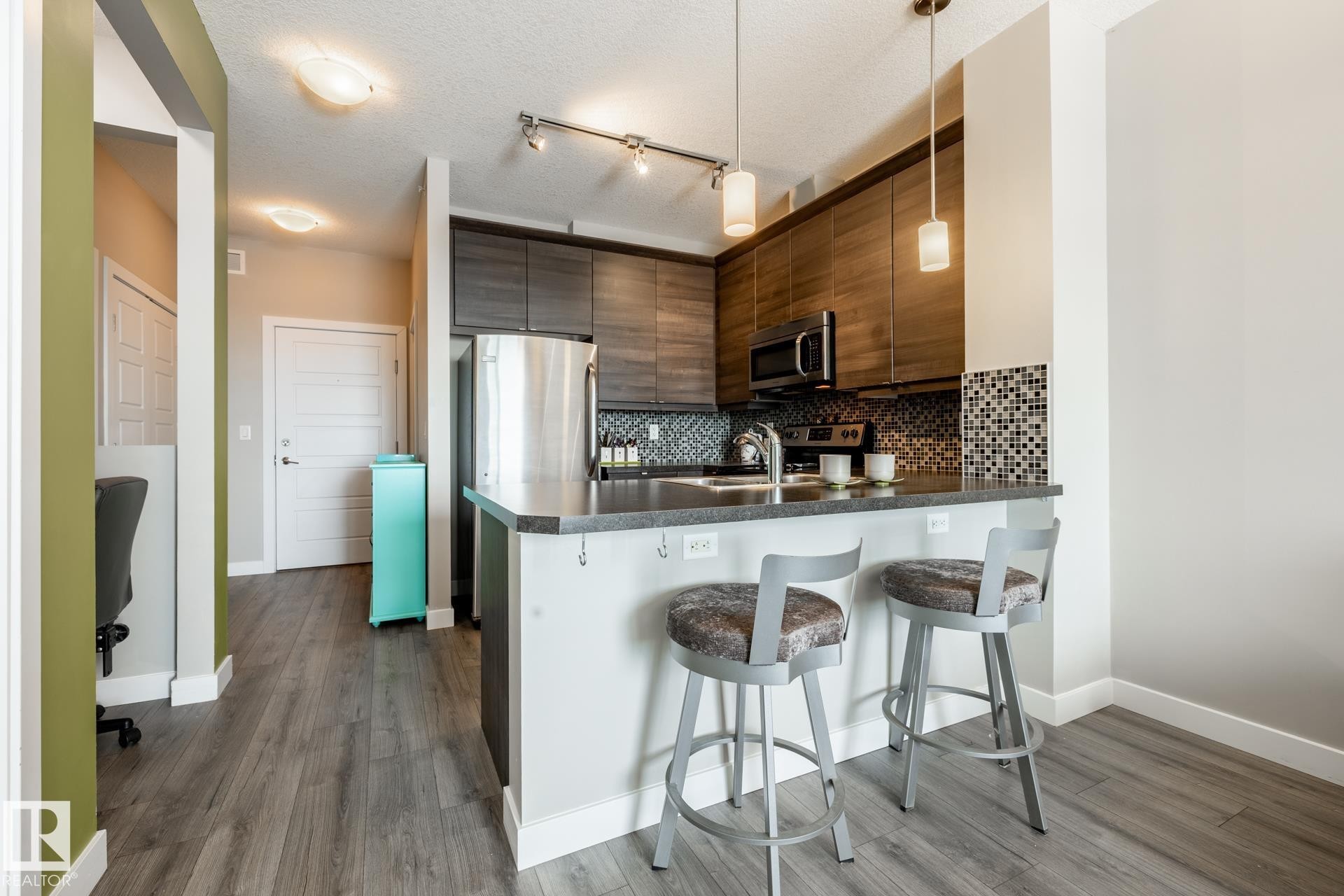 Kitchen featuring a peninsula, stainless steel appliances, a kitchen breakfast bar, dark wood-type flooring, and a textured ceiling - 407 2590 Anderson Way, Edmonton, AB - Indoor Photo Showing Kitchen With Upgraded Kitchen
