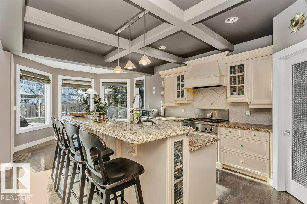 Kitchen with glass insert cabinets, light stone countertops, pendant lighting, tasteful backsplash, and coffered ceiling - 1579 Hector Road, Edmonton, AB - Indoor