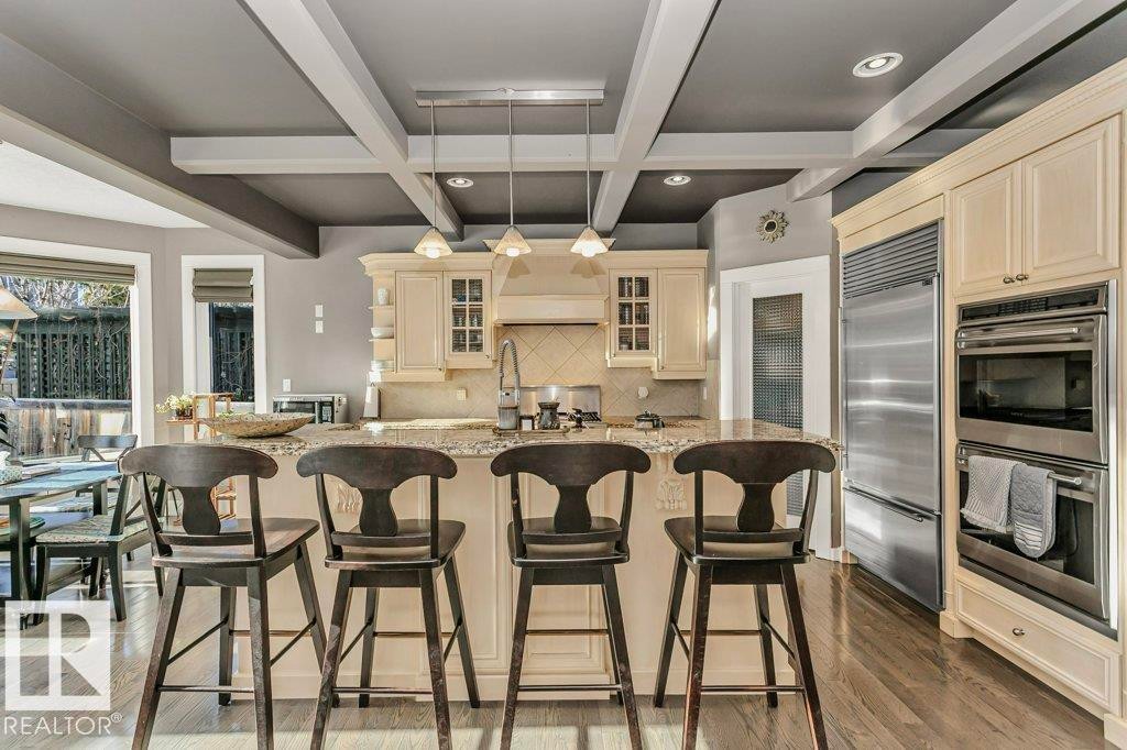 Kitchen with glass insert cabinets, stainless steel appliances, decorative light fixtures, coffered ceiling, and cream cabinetry - 1579 Hector Road, Edmonton, AB - Indoor