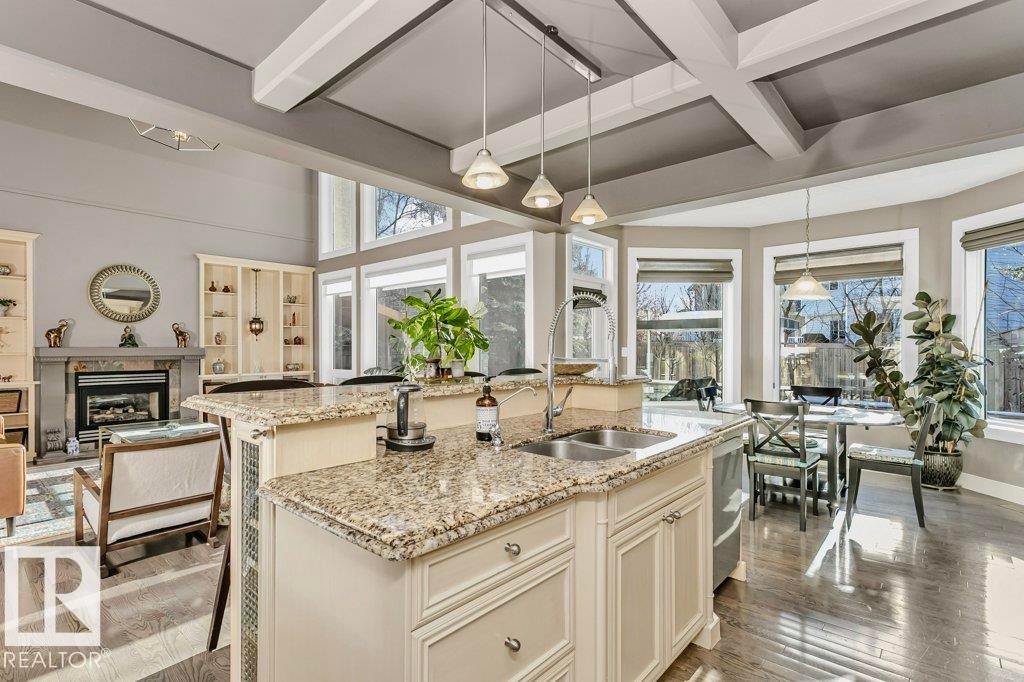 Kitchen with light stone countertops, pendant lighting, light wood-type flooring, beam ceiling, and a kitchen island with sink - 1579 Hector Road, Edmonton, AB - Indoor Photo Showing Kitchen With Double Sink