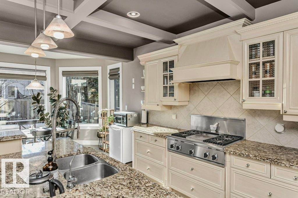 Kitchen featuring cream cabinetry, glass insert cabinets, stainless steel appliances, pendant lighting, and light stone counters - 1579 Hector Road, Edmonton, AB - Indoor Photo Showing Kitchen With Double Sink With Upgraded Kitchen