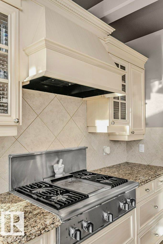 Kitchen featuring glass fronted cabinets, light stone counters, cream cabinets, gas stove, and tasteful backsplash - 1579 Hector Road, Edmonton, AB - Indoor Photo Showing Kitchen With Upgraded Kitchen
