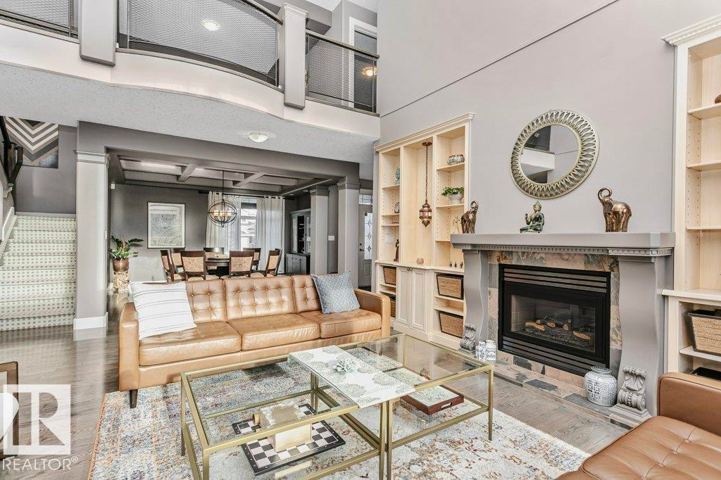 Living area featuring built in features, a glass covered fireplace, wood finished floors, suspended lighting, and a high ceiling - 1579 Hector Road, Edmonton, AB - Indoor Photo Showing Living Room With Fireplace