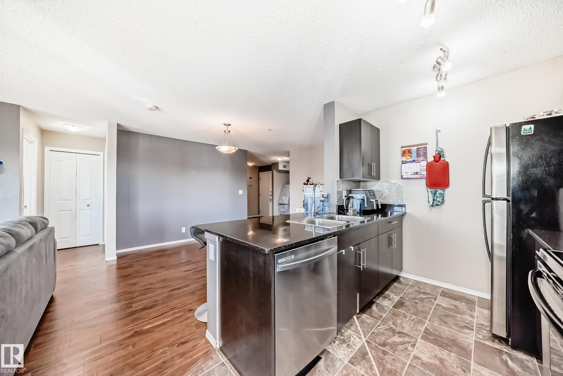 Kitchen with open floor plan, dishwasher, a peninsula, decorative light fixtures, and a textured ceiling - 302 530 Watt Boulevard Sw, Edmonton, AB - Indoor Photo Showing Kitchen With Stainless Steel Kitchen