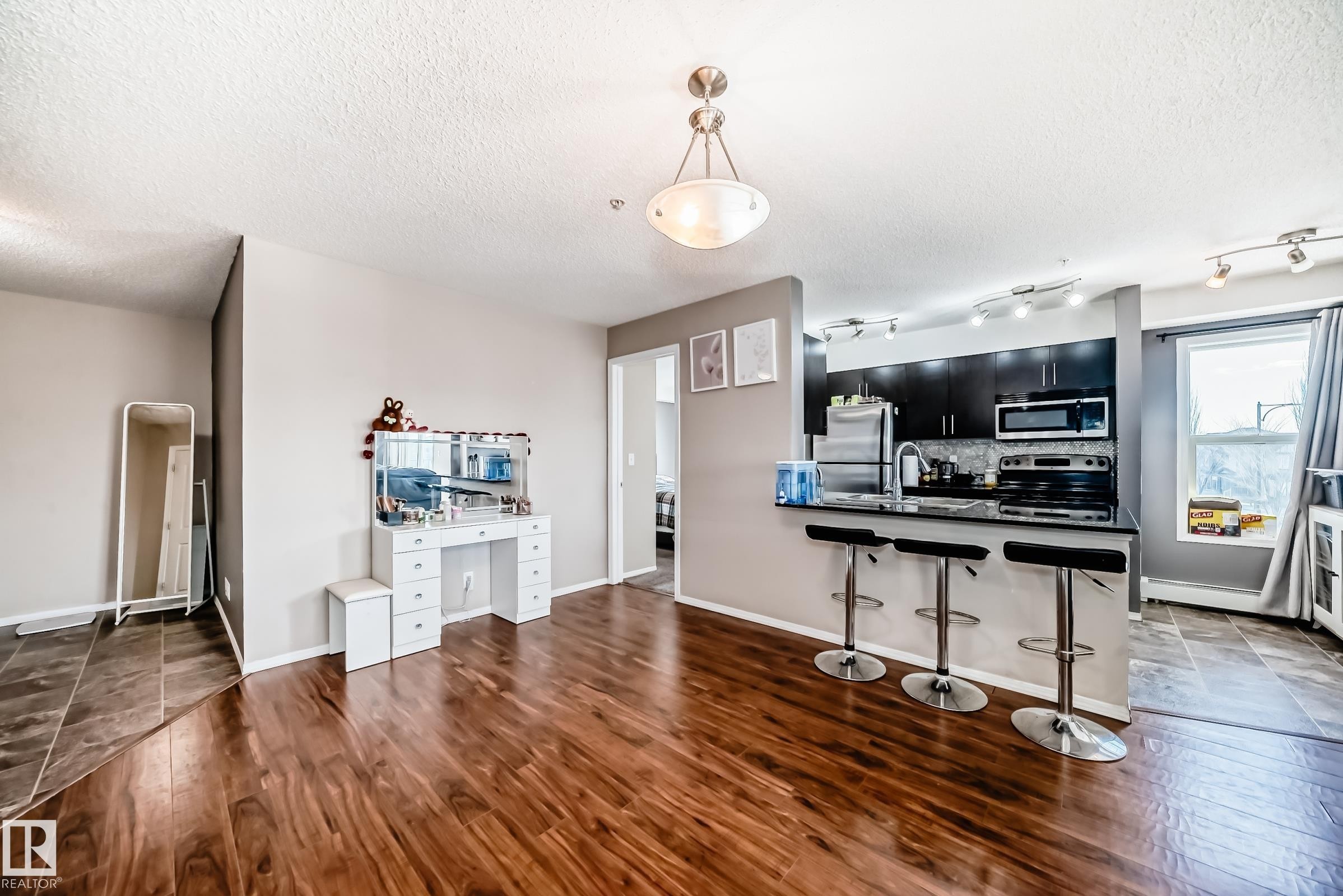 Kitchen featuring dark cabinets, a kitchen bar, hanging light fixtures, a peninsula, and a textured ceiling - 302 530 Watt Boulevard Sw, Edmonton, AB - Indoor Photo Showing Other Room