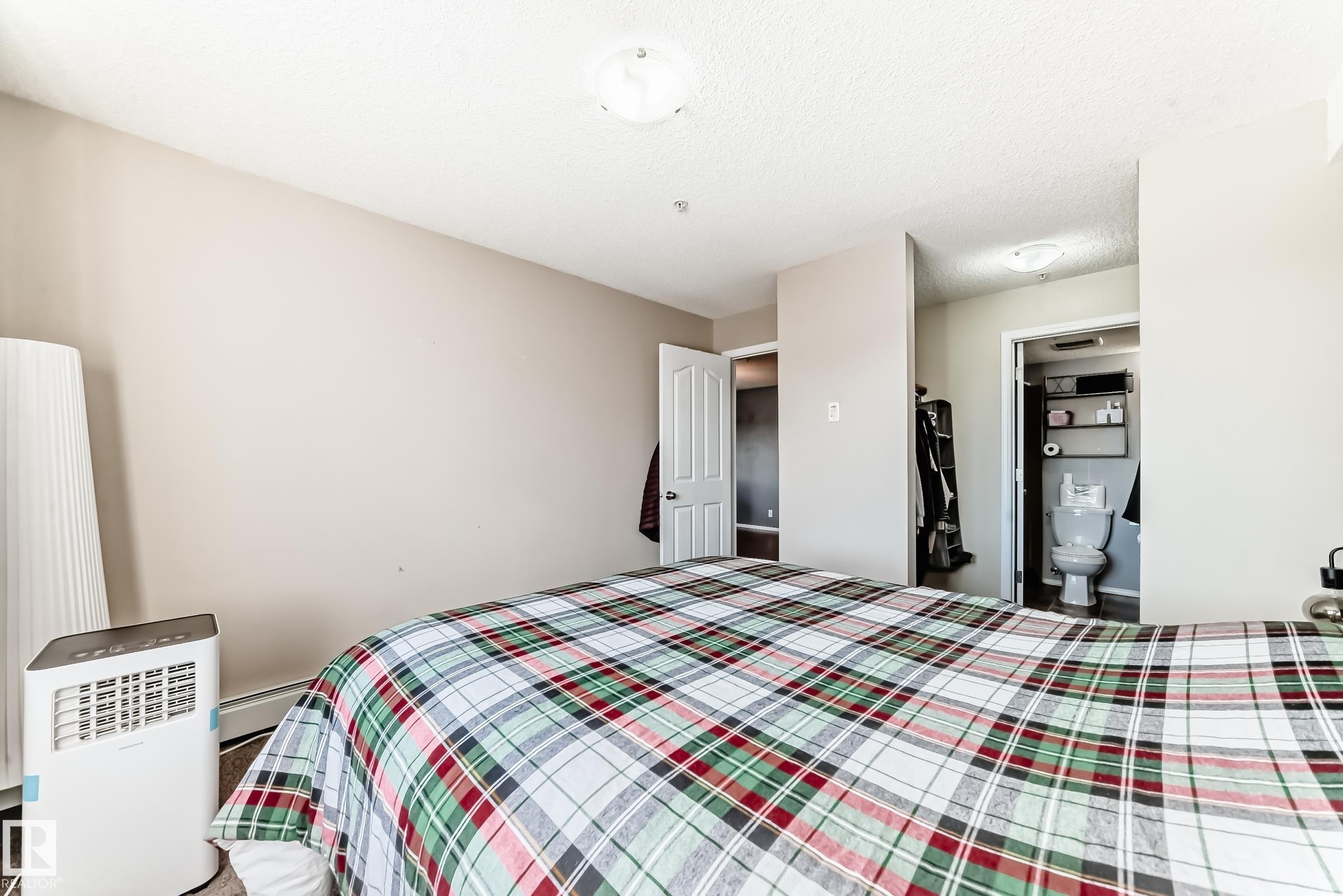 Bedroom with a baseboard heating unit, a textured ceiling, and connected bathroom - 302 530 Watt Boulevard Sw, Edmonton, AB - Indoor Photo Showing Bedroom